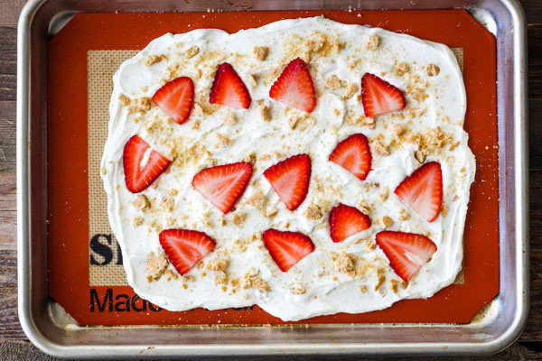 Yogurt spread onto a silicone baking mat topped with strawberries and graham cracker.