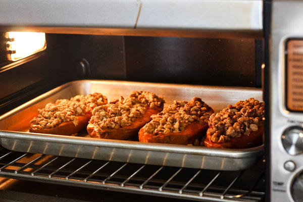 Sweet potatoes on a baking sheet in a countertop oven.