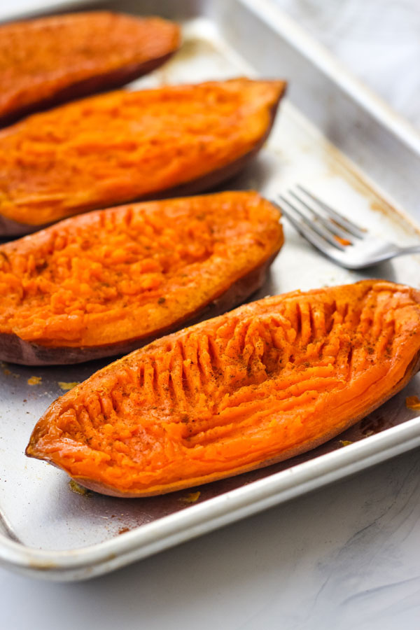 Cooked sweet potato halves on a quarter sheet pan.