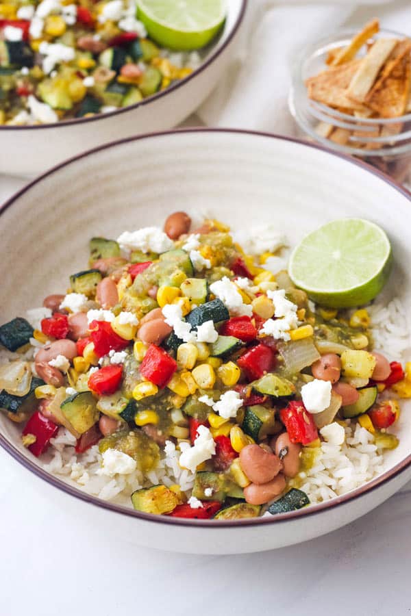 Close up of bowl with savory roasted veggies, salsa, pinto beans, rice, and half a lime.