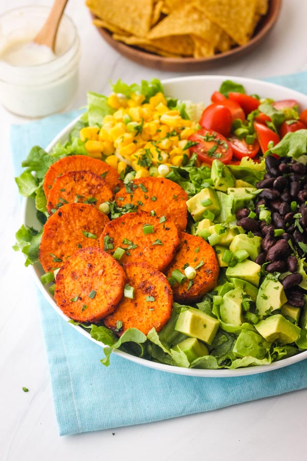 Bowl of salad with sweet potato slices, avocado, black beans, and corn.