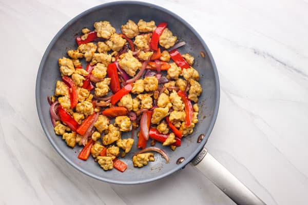 Skillet with browned tempeh chunks and pieces of red pepper and onion.