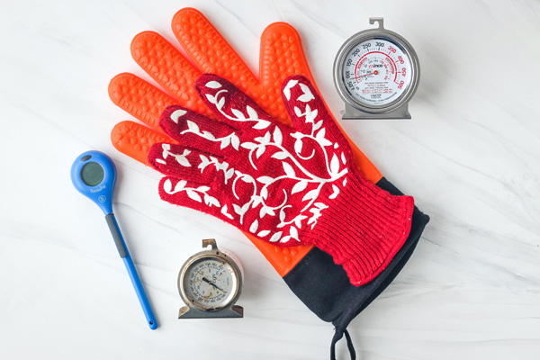 Oven thermometers, orange and red oven gloves, and an instant read thermometer.