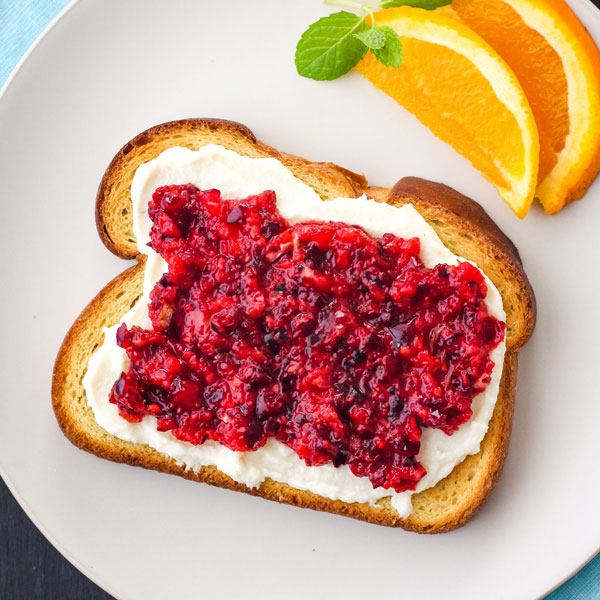 Toasted bread spread with creamy whipped ricotta and cranberry raspberry relish on a blue plate.