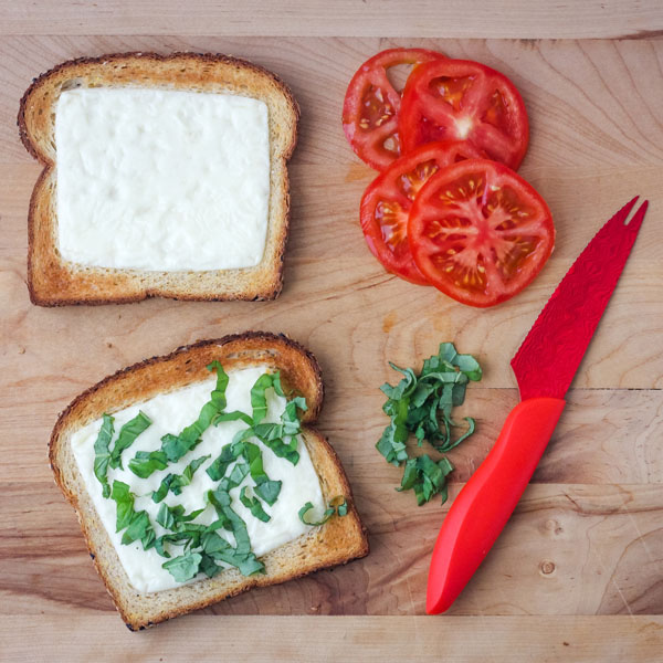 Cheesy toasted bread and tomato slices on a cutting board.