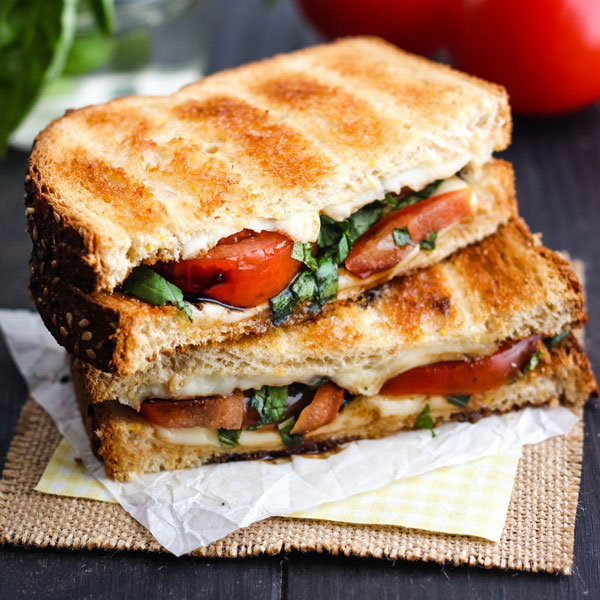 Toasted Caprese Sandwich sliced in half on a piece of parchment.