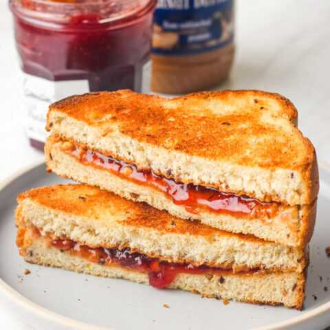 Toasted peanut butter and jelly sandwich slices stacked on a blue plate.