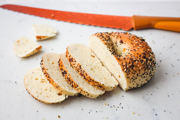 Everything bagel sliced on a cutting board with an orange knife.