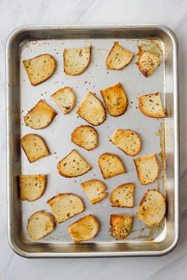 Overhead view of toasted bagel chips on a quarter sheet pan.