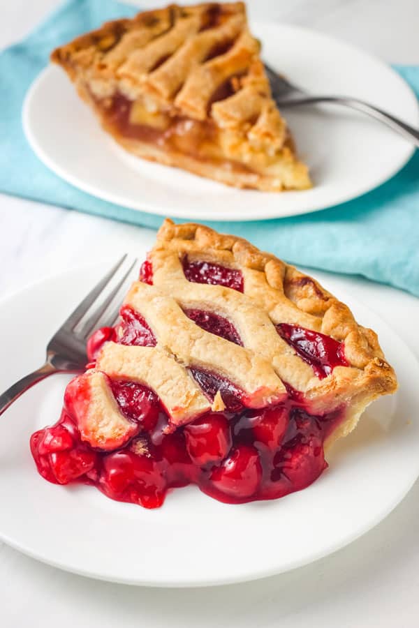 Plates with slices of cherry pie and apple pie on a table.