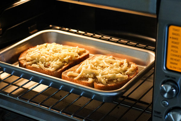 Bread slices with cheese on a baking sheet inside a toaster oven.