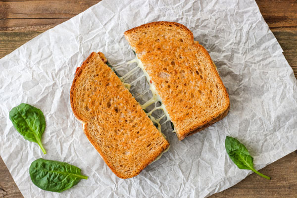 Grilled cheese sandwich split in half and pulled apart on a piece of white parchment paper.