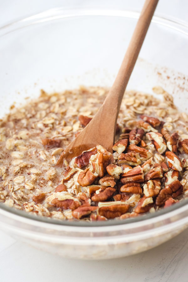 Oatmeal ingredients in a glass mixing bowl with a wooden spoon.