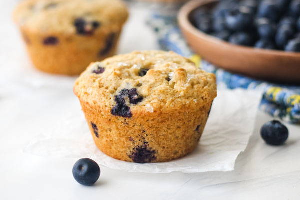 Blueberry Muffins on a table with a bowl of fresh blueberries.