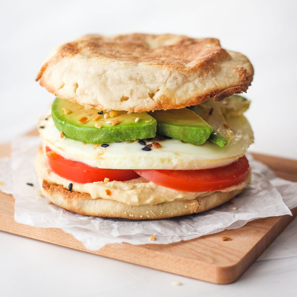 English muffin topped with egg and hummus on small cutting board.