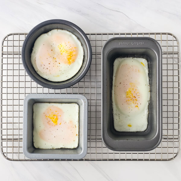 Eggs baked in a small round pan, square pan, and mini muffin pan on a baking rack. 