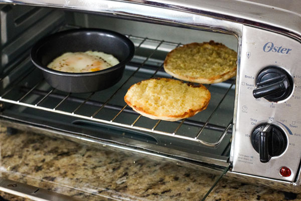 Cooked egg and toasted English muffin halves inside a toaster oven.