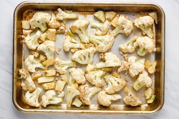 Seasoned cauliflower spread out on a rimmed sheet pan.