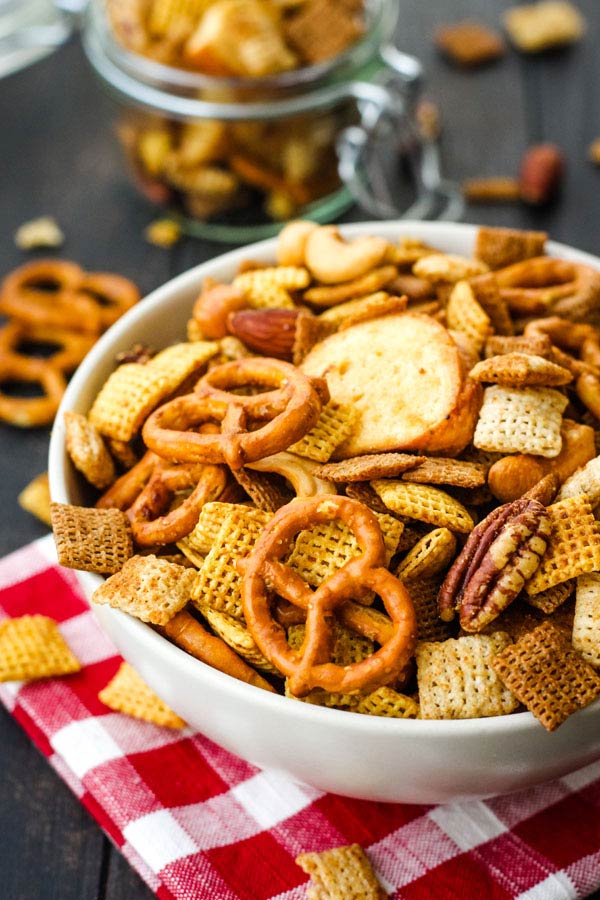 Chex mix in a white bowl on a red checkered napkin.