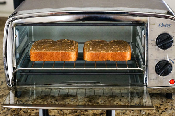 Two slices of bread on a rack inside a toaster oven.