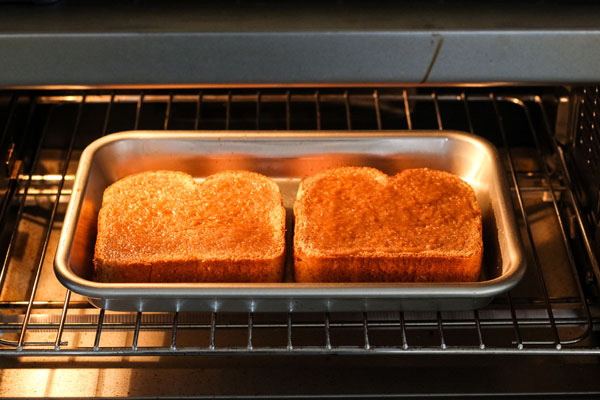 Bread slices on a baking sheet inside a countertop oven.