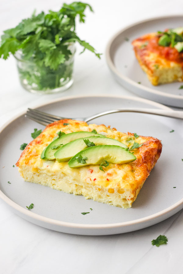 Slice of egg bake with avocado slices on a blue plate.