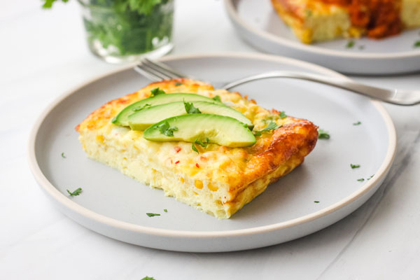 A slice of egg casserole on a blue plate with a fork.