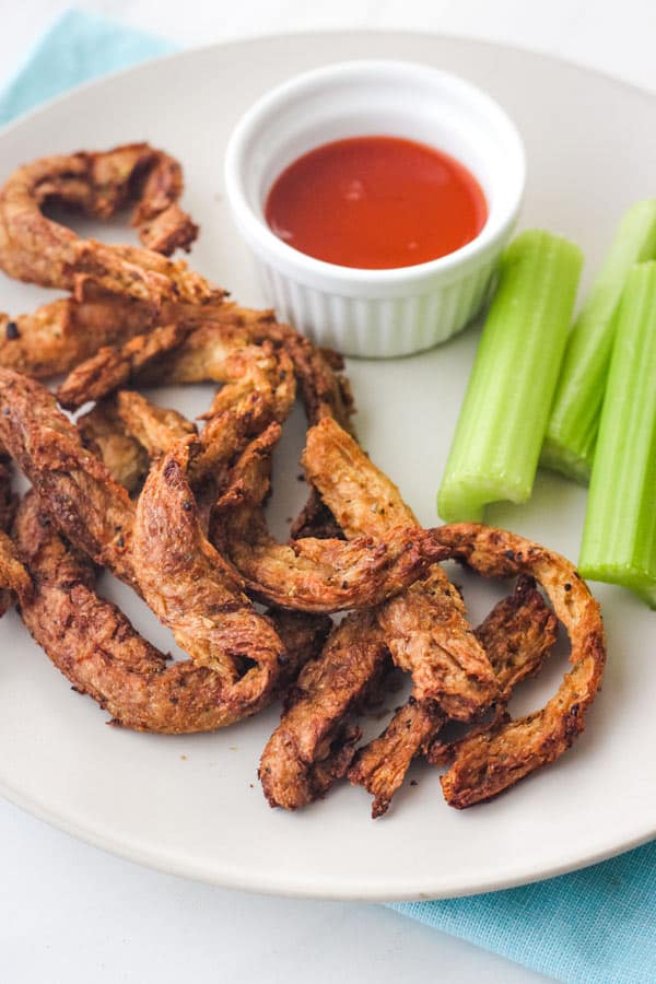 Seasoned soy curls on a plate with ramekin of buffalo sauce.