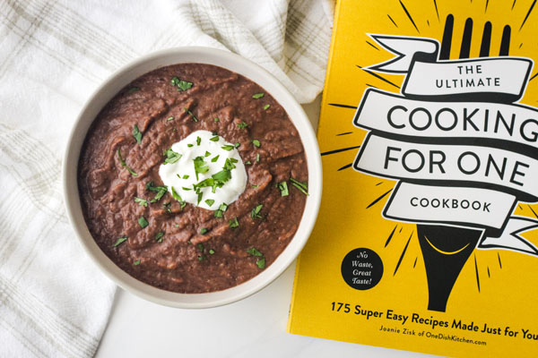 Black bean soup in a white bowl next to a cooking for one cookbook.