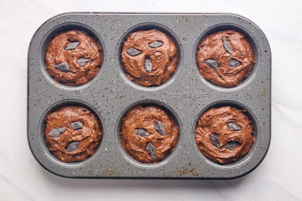 Batter in muffin pan topped with chocolate chunks.