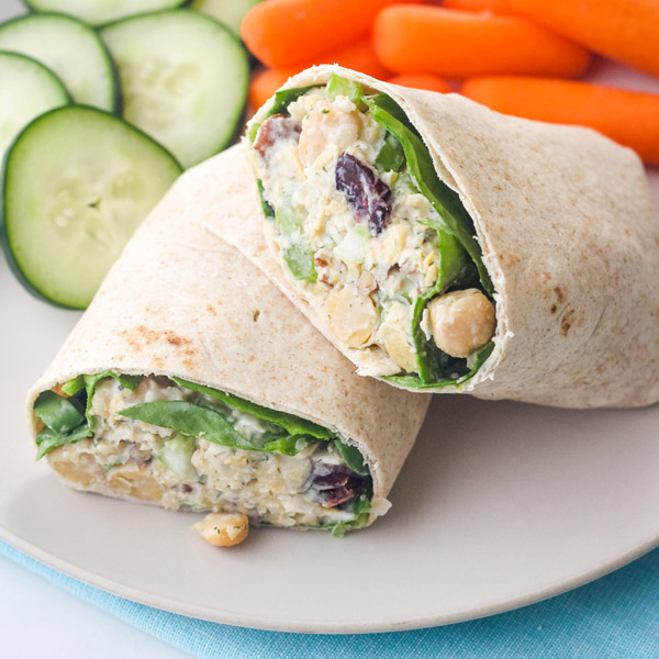 Chickpea wrap on a plate with cucumber slices and baby carrots.