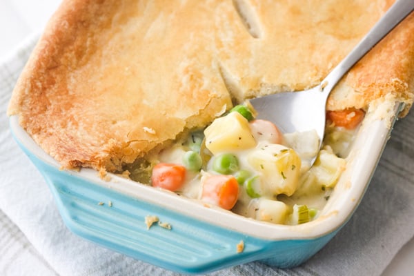 Closeup of spoon scooping creamy vegetables and pie crust in a baking dish.