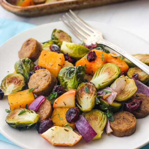 A tan plate full of roasted vegetables and vegetarian sausage on a blue napkin.