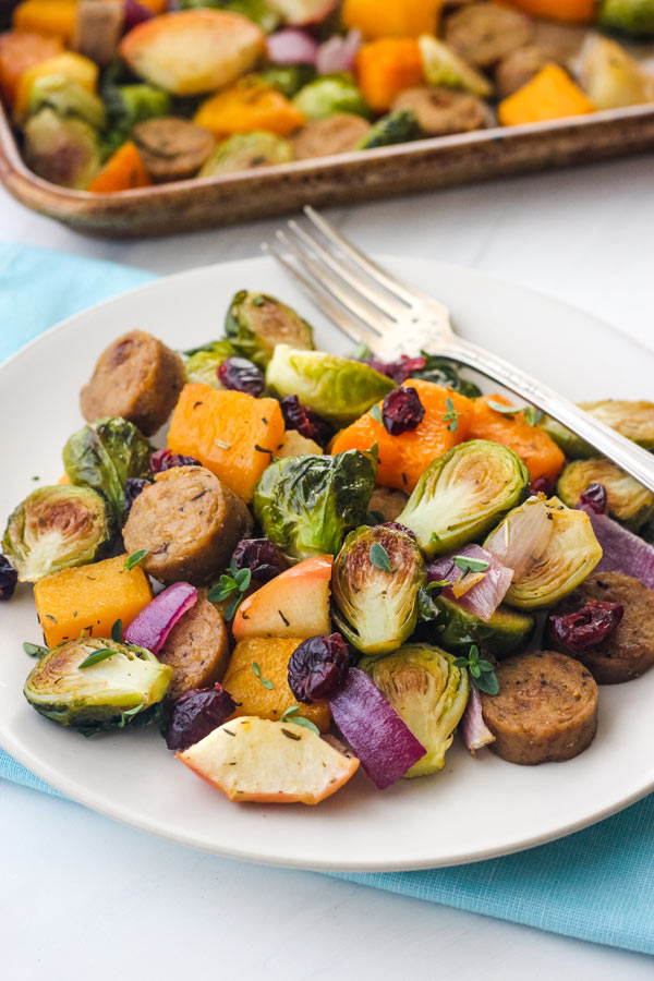 A tan plate full of roasted vegetables and vegetarian sausage on a blue napkin.