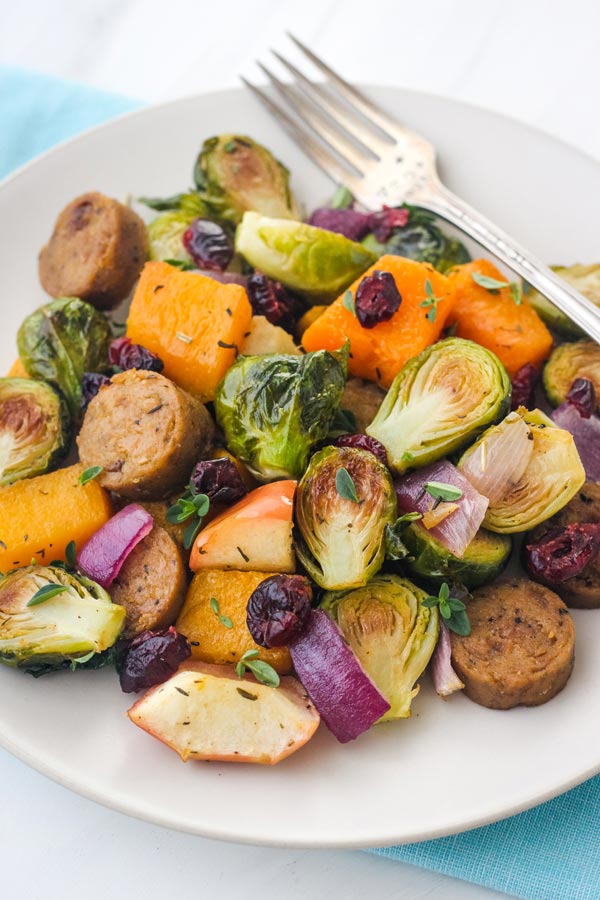 Closeup of roasted Brussels sprouts, apple chunks, butternut squash, and vegetarian sausage sprinkled with dried cranberries. 