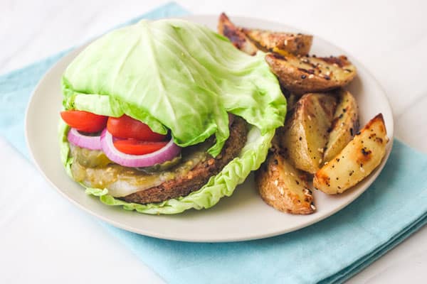 Plate with potato wedges and a veggie burger wrapped in cabbage buns.