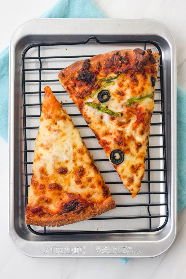 Overhead view of warmed cheese and veggie pizza slices on a mini rack inside a small pan.