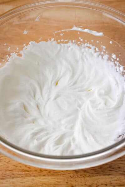 A glass bowl of whipped cream with medium peaks.
