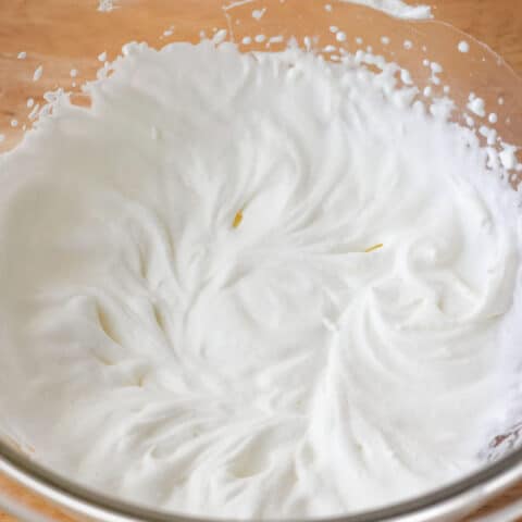 A glass bowl of whipped cream with medium peaks.