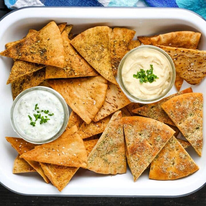 White baking dish with a variety of seasoned pita chips and dips in small mason jars.