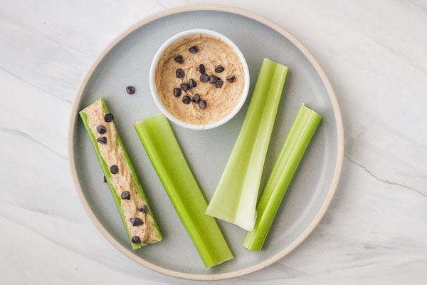 Celery sticks on a plate with a white bowl of yogurt dip.