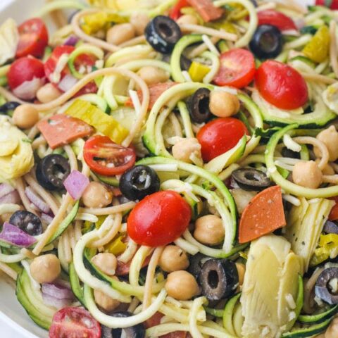 Closeup of a tossed zucchini pasta salad in a large white bowl.