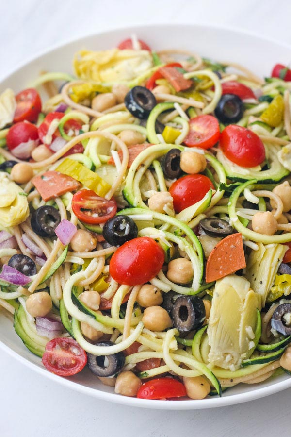 Closeup of a tossed zucchini pasta salad in a large white bowl. 