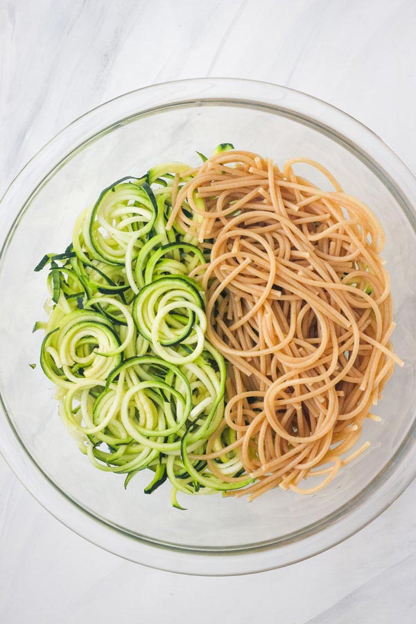 Zucchini noodles and cooked spaghetti noodles in a glass bowl.