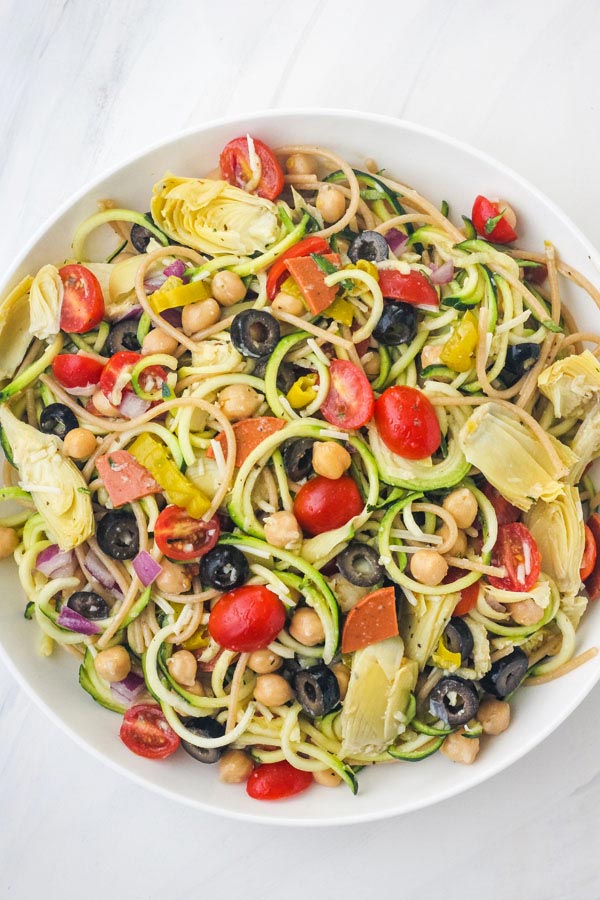 Overhead view of a big bowl of zucchini pasta salad on a white table. 