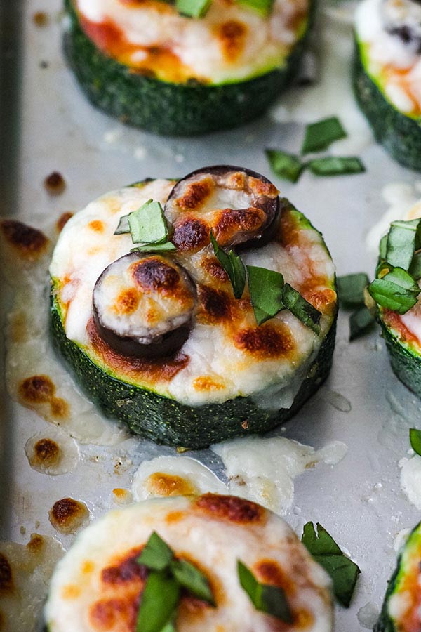 Baked zucchini bites with melted cheese and black olive slices sprinkled with fresh basil.