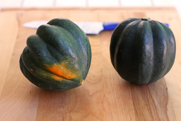 two acorn squashes on a cutting board with a knife