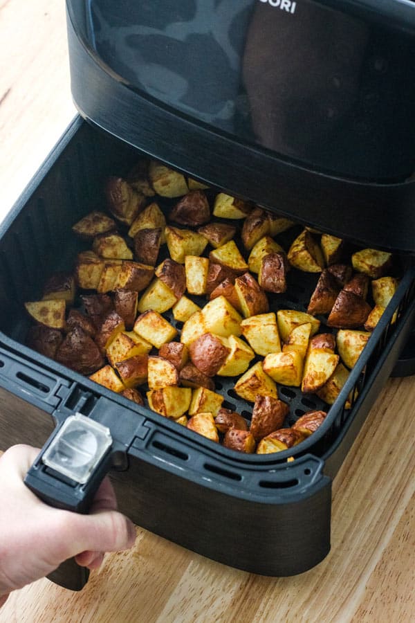 Hand pulling drawer of roasted potatoes from an air fryer.