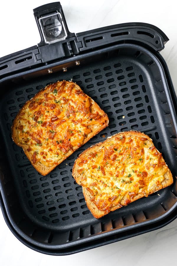 Overhead view of two browned cheesy toast inside an air fryer basket.