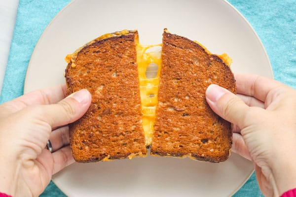 Hands pulling apart a split grilled cheese sandwich.